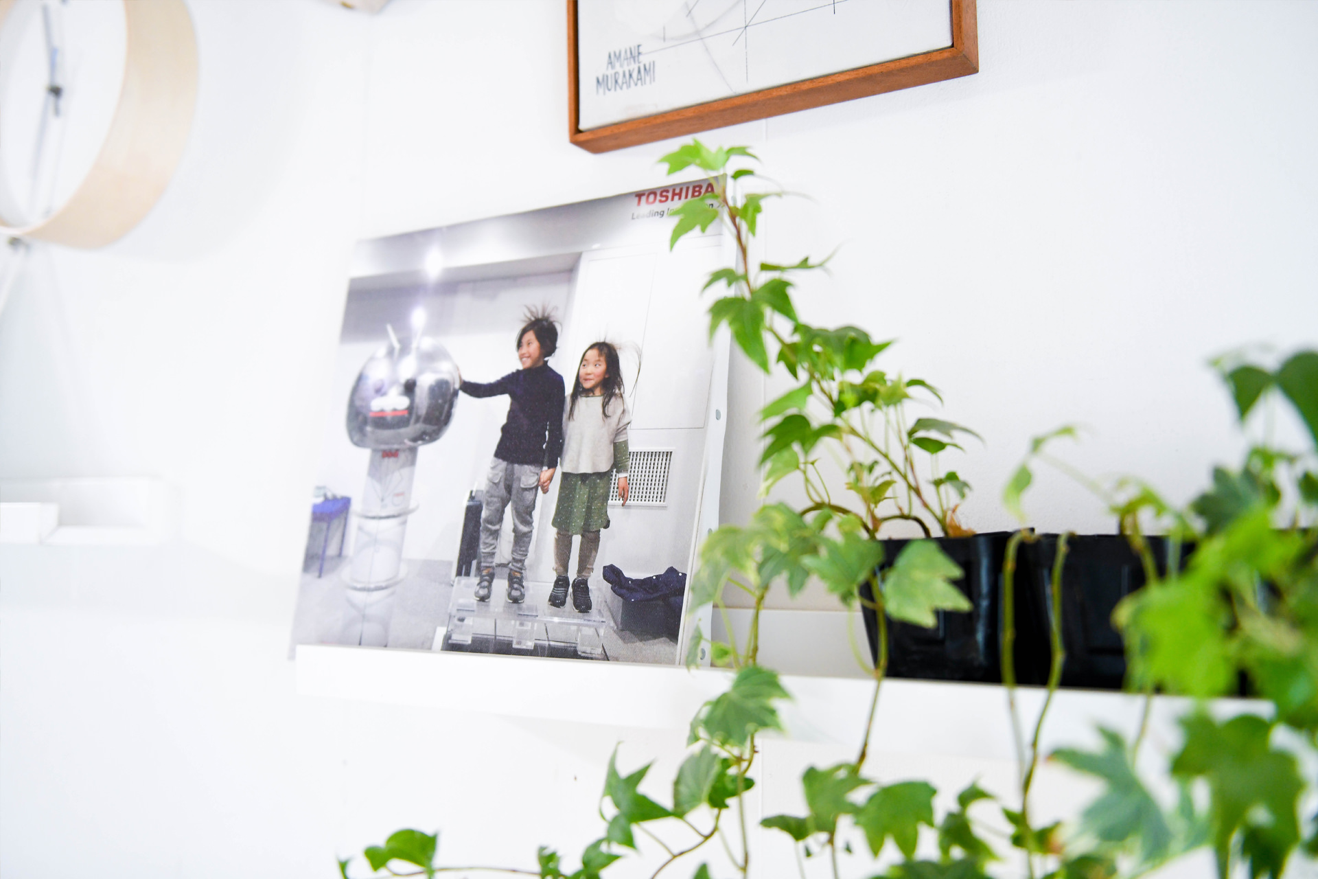 植物の陰に置かれた、二人の子どもが写るWALL DECOR。