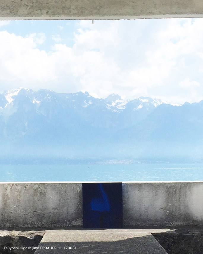 雪の残る険しい山々と青い海を背景に、コンクリートの縁に置かれたTsuyoshi Higashijimaの青い抽象画の作品。