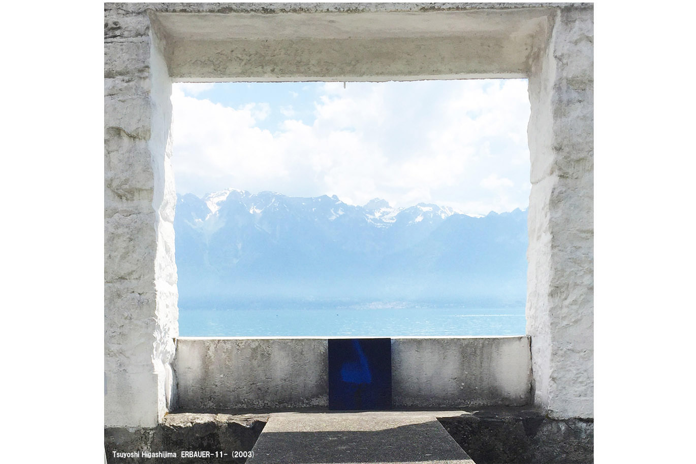 雪の残る険しい山々と青い海を背景に、コンクリートの縁に置かれたTsuyoshi Higashijimaの青い抽象画の作品。