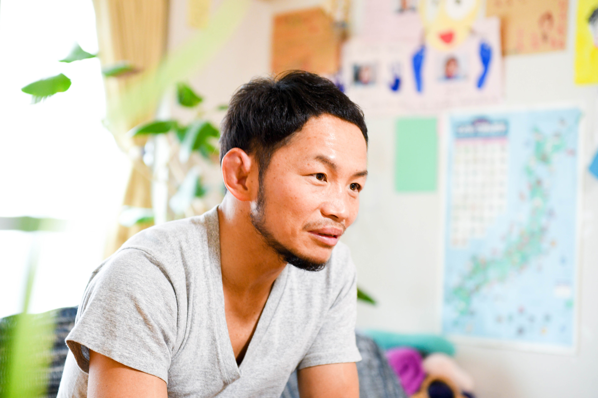 壁に多くの写真やメモが貼られた、クリエイティブな雰囲気のワークスペースに座る男性。