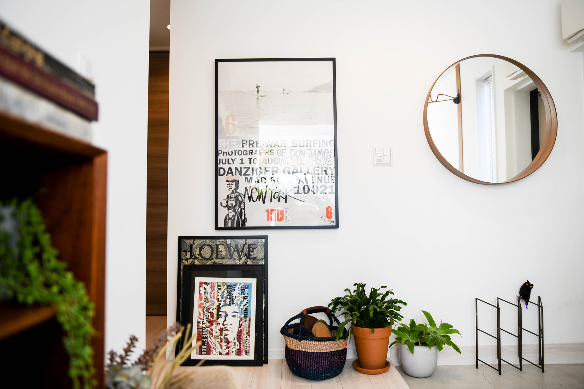 サーフィンの写真とタイポグラフィがデザインされた大きなアートポスター。その下の床面には、LOEWEのアートフレームや観葉植物、バスケットが並ぶモダンなインテリアの壁面。