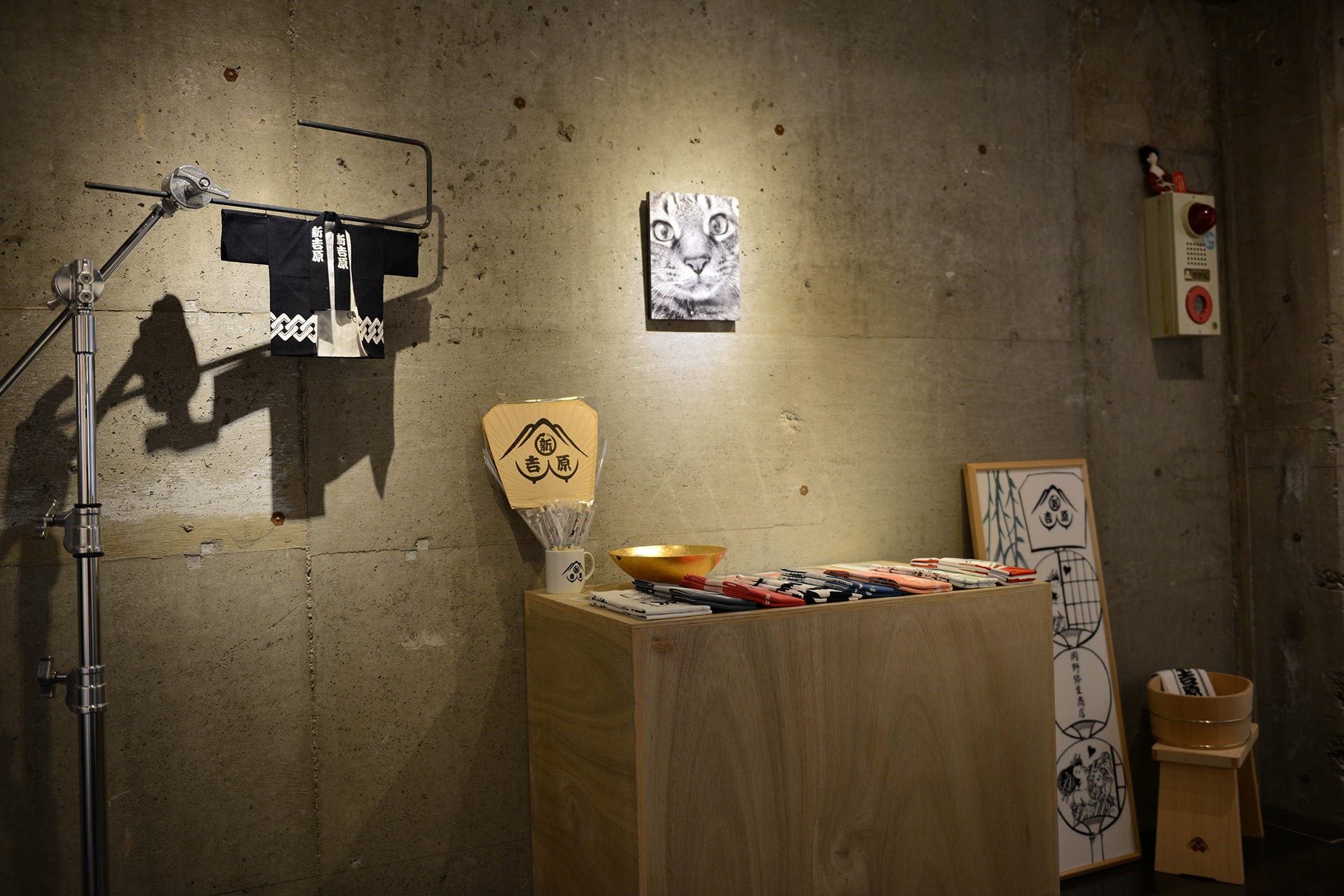 コンクリート壁の前に、ミニチュアの法被や猫のWALL DECOR カジュアル、団扇などがディスプレイされた什器が並ぶショップの風景。右端には木製の湯桶やアートボードも見える。