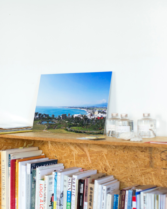 本が並ぶ棚の上に、青い海と街並みの風景のWALL DECOR ミュージアムを飾る。