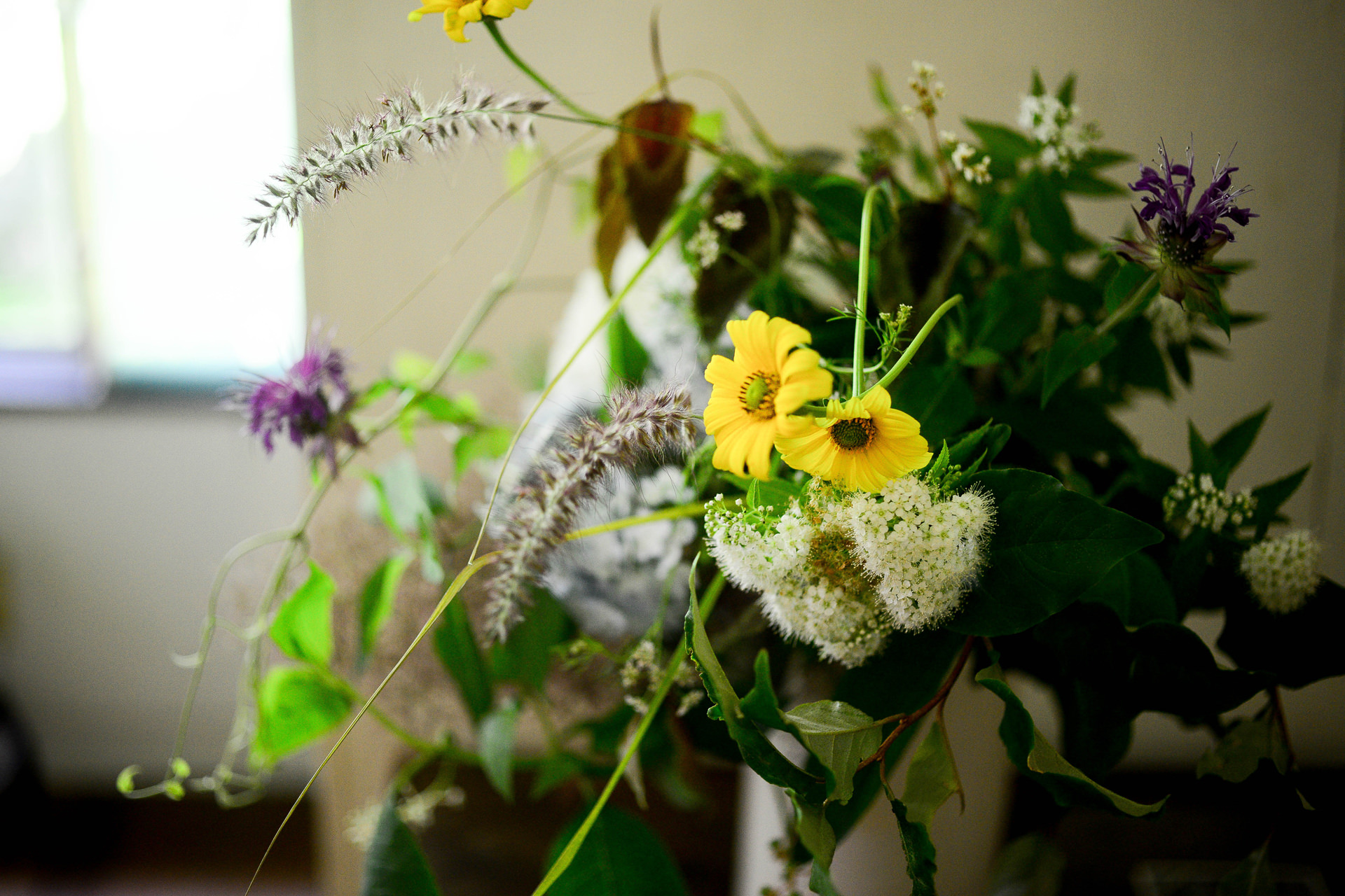 黄色いデイジーや白い小花、紫の草花をナチュラルに活けたフラワーアレンジメント。