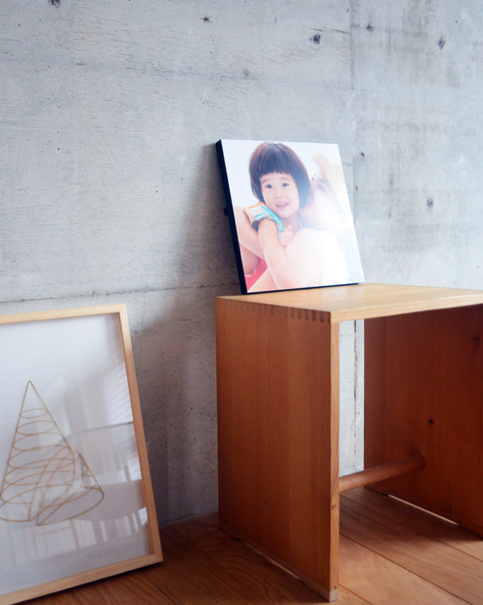 コンクリートの壁を背景に、木の台に飾られた子供の写真のWALL DECOR カジュアルと、床に置かれた額縁。