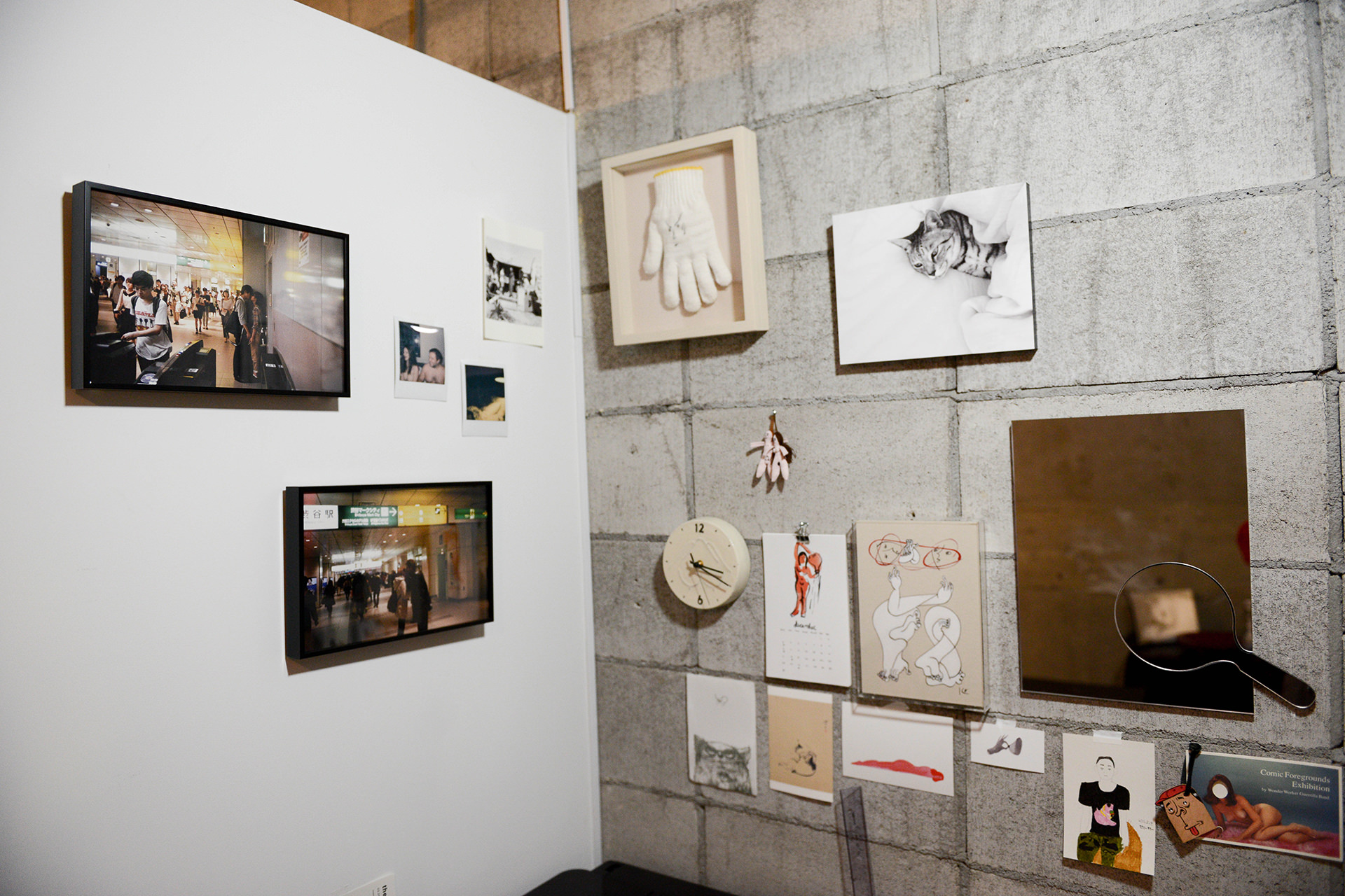 白い壁とコンクリート壁が交差する一角に、駅の風景写真や額装された白い軍手、猫のWALL DECOR カジュアル、多彩なイラストなどがコラージュのように飾られたアトリエの風景。