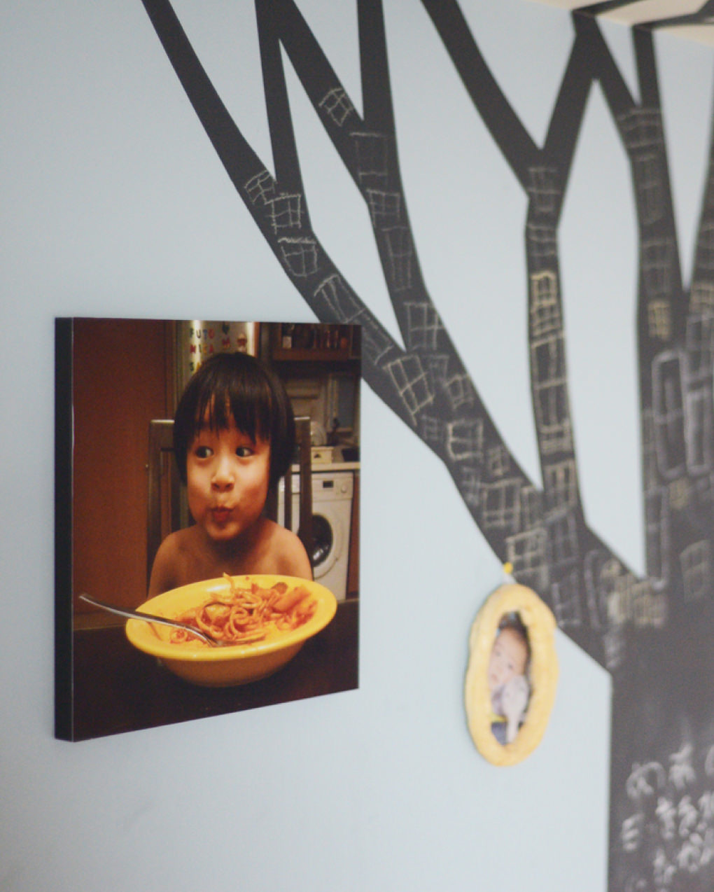 黒い木のイラストが描かれた壁に、パスタを食べる子供の写真のWALL DECORを飾る。