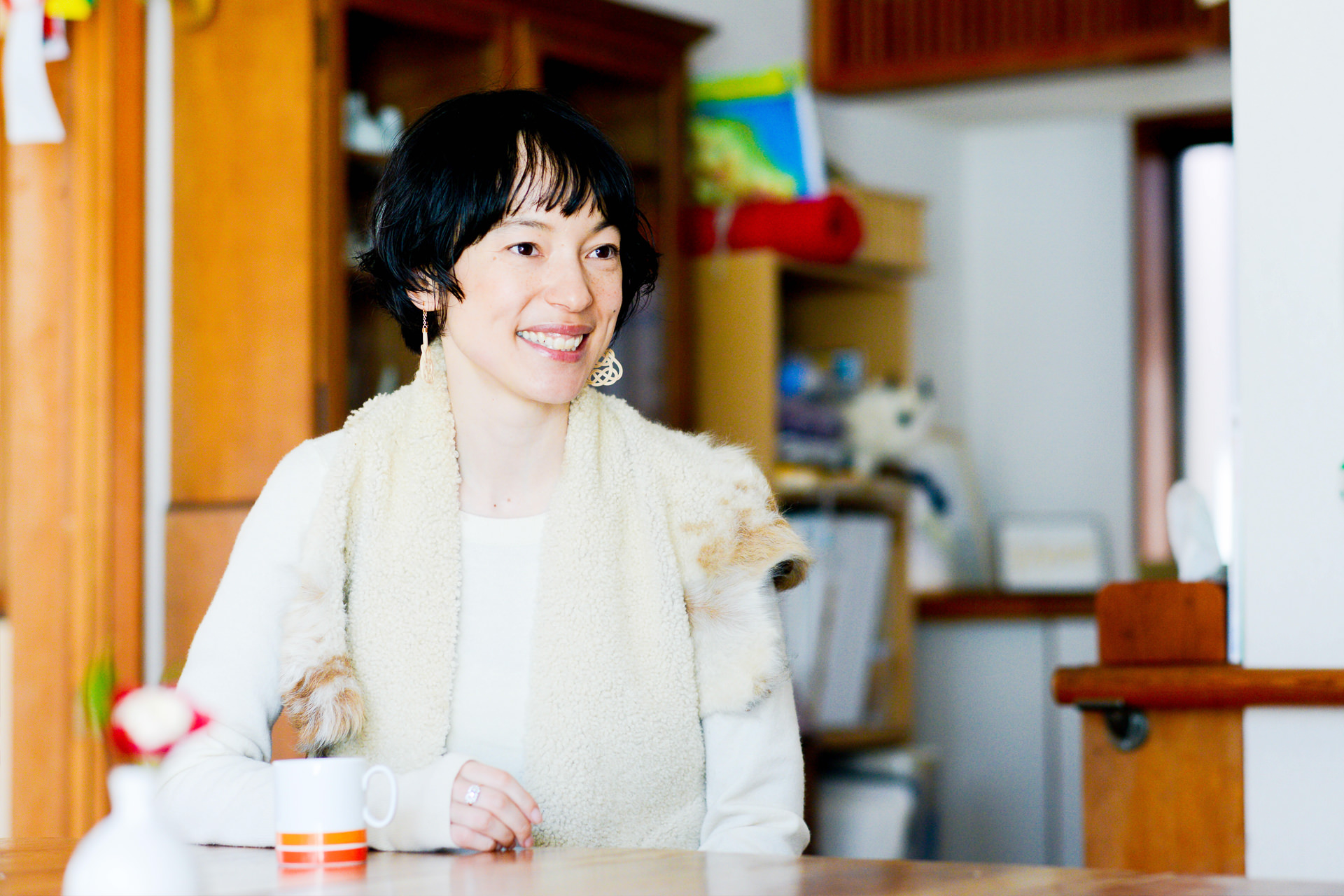 白い服を着用し、リラックスした表情で佇む女性。背景には和室の調度品が見える。