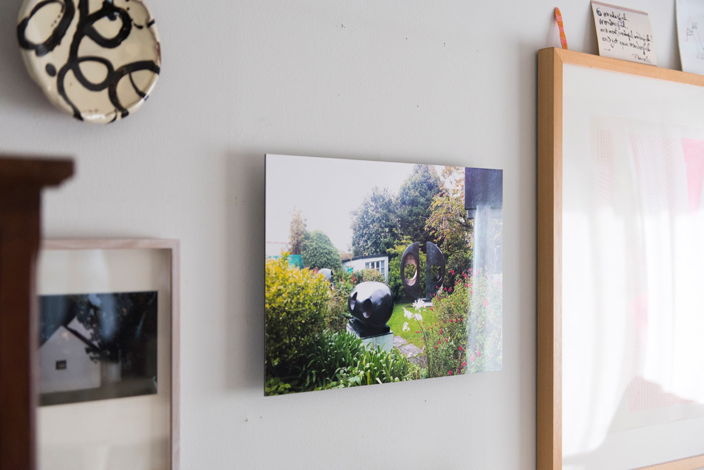 お皿のオブジェや他の額縁とともに白い壁に飾られた、庭園にある彫刻作品の写真のWALL DECOR ミュージアム