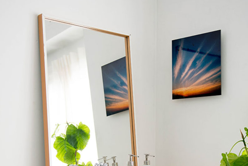 白い壁に飾られた、美しい夕焼け空と筋状の雲の写真のWALL DECOR ミュージアム。隣にある大きな鏡にその姿が映り込んでいる。