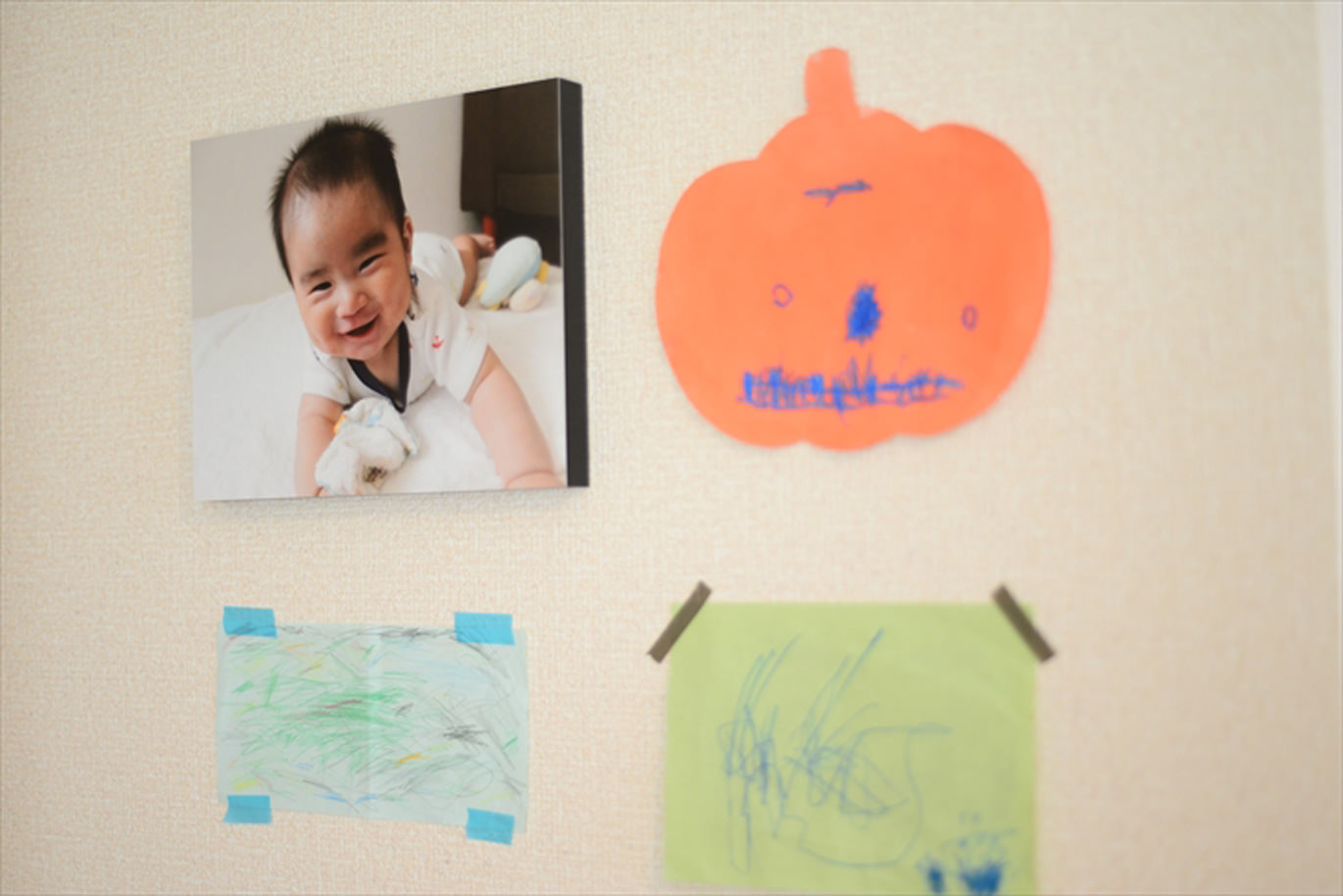 子供が描いた絵とともに壁に飾られた、うつ伏せで笑う赤ちゃんの写真のWALL DECOR カジュアル
