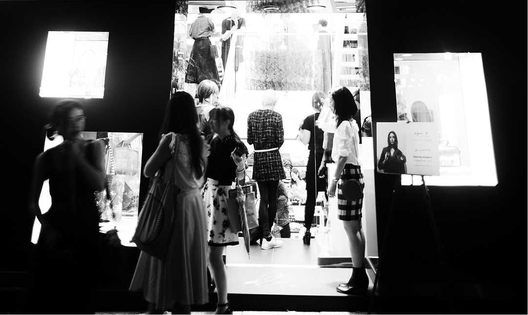 モノクロで表現された、賑わうギャラリーやショップの入り口付近の光景。右端には「agnès b.」のロゴが入ったイベントの案内板が立てられ、多くの人々が集まっている。