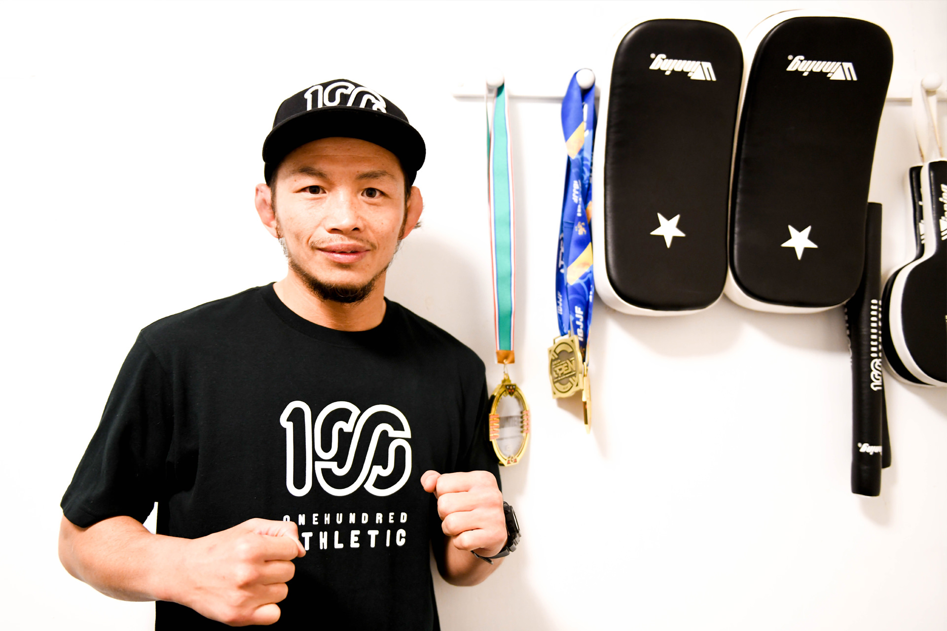 壁にグローブやメダルが整然と並ぶ部屋に、黒いTシャツ姿で立つ山野辺氏。