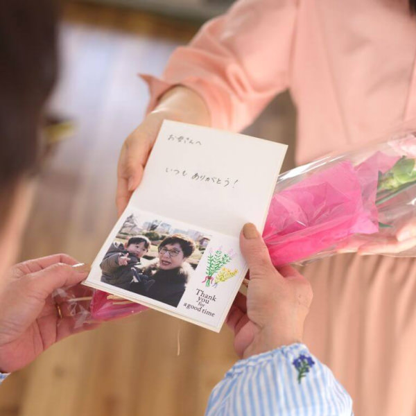 写真とメッセージが添えられたカードと花束を、お母さんへ手渡している様子。