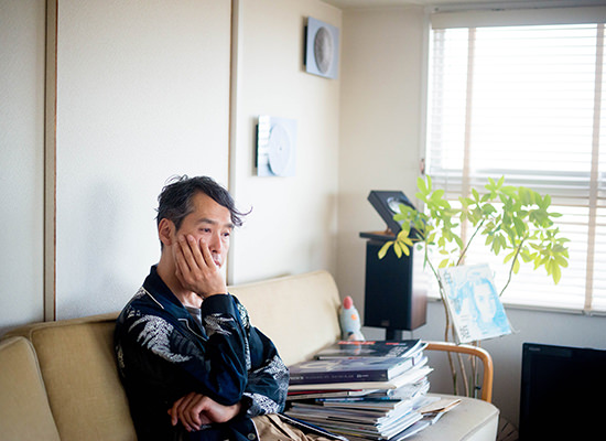 ソファーで頬杖をつく男性と、壁に飾られた円形アートのWALL DECOR ミュージアム。観葉植物や本が並ぶ落ち着いた室内の風景。