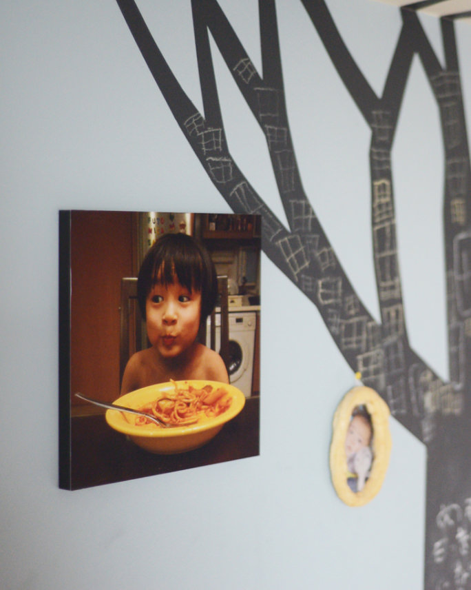 黒い木のイラストが描かれた壁に、パスタを食べる子供の写真のWALL DECOR カジュアルを飾る。
