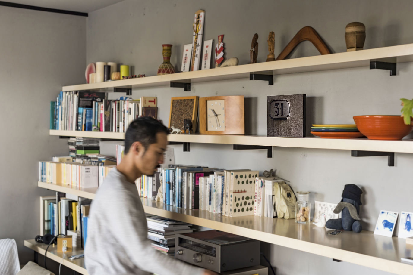 棚に並ぶ本と装飾品のある部屋で作業する男性