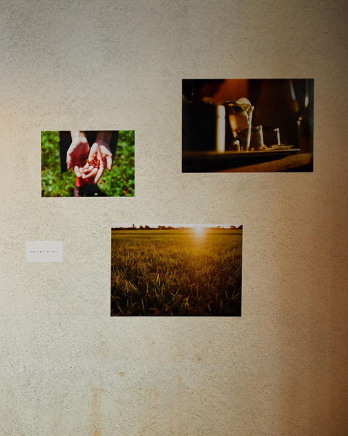 ベージュの壁に、赤い実を乗せた両手、グラス、夕暮れの田園風景といった3枚の写真パネルがバランスよく飾られている。