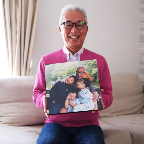 孫たちとの写真がプリントされたWALL DECORを持ち、笑顔のおじいちゃん。
