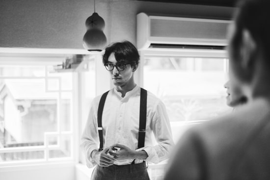 今泉悠。手前には別の人影がぼけて写り込み、背景には明るい窓がある風景。