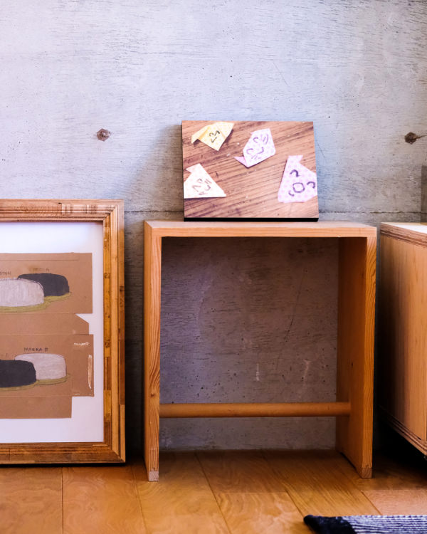 コンクリートの壁を背景に、床に置かれた額縁と、木の台に飾られた折り紙のWALL DECOR。