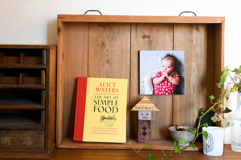 木製の棚に飾られた、赤ちゃんの写真のWALL DECOR カジュアル。黄色い本や小物と一緒にディスプレイされている。