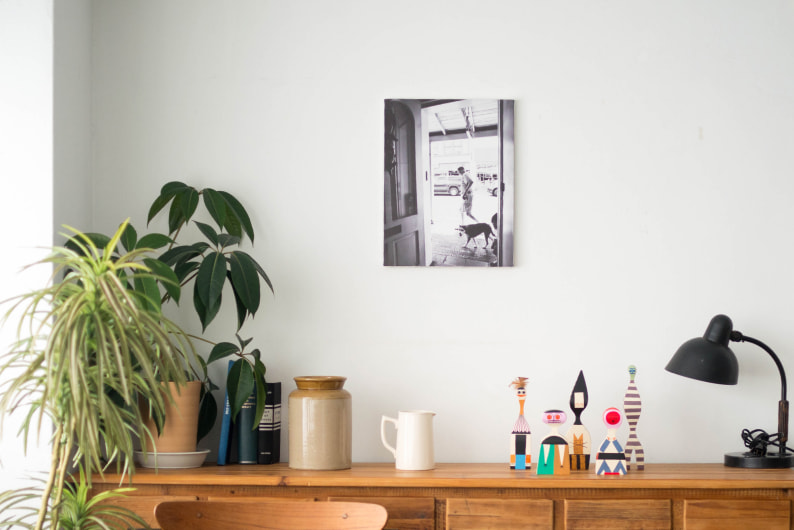 木製の棚の上に飾られた、犬と人が写るモノクロ写真のWALL DECOR キャンバス。観葉植物や個性的な置物が並ぶ空間に馴染んでいる。