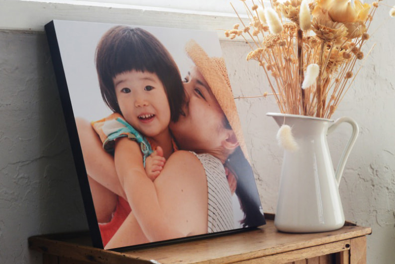 木製の棚に飾られた、親子の微笑ましい写真のWALL DECOR カジュアル。ドライフラワーを活けた白い花瓶が隣に添えられている。
