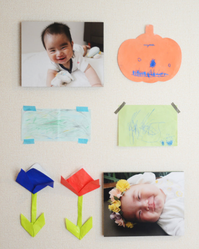 白い壁に飾られた、2枚の赤ちゃんの写真のWALL DECOR カジュアルと、子供の絵や折り紙のチューリップなどの作品。