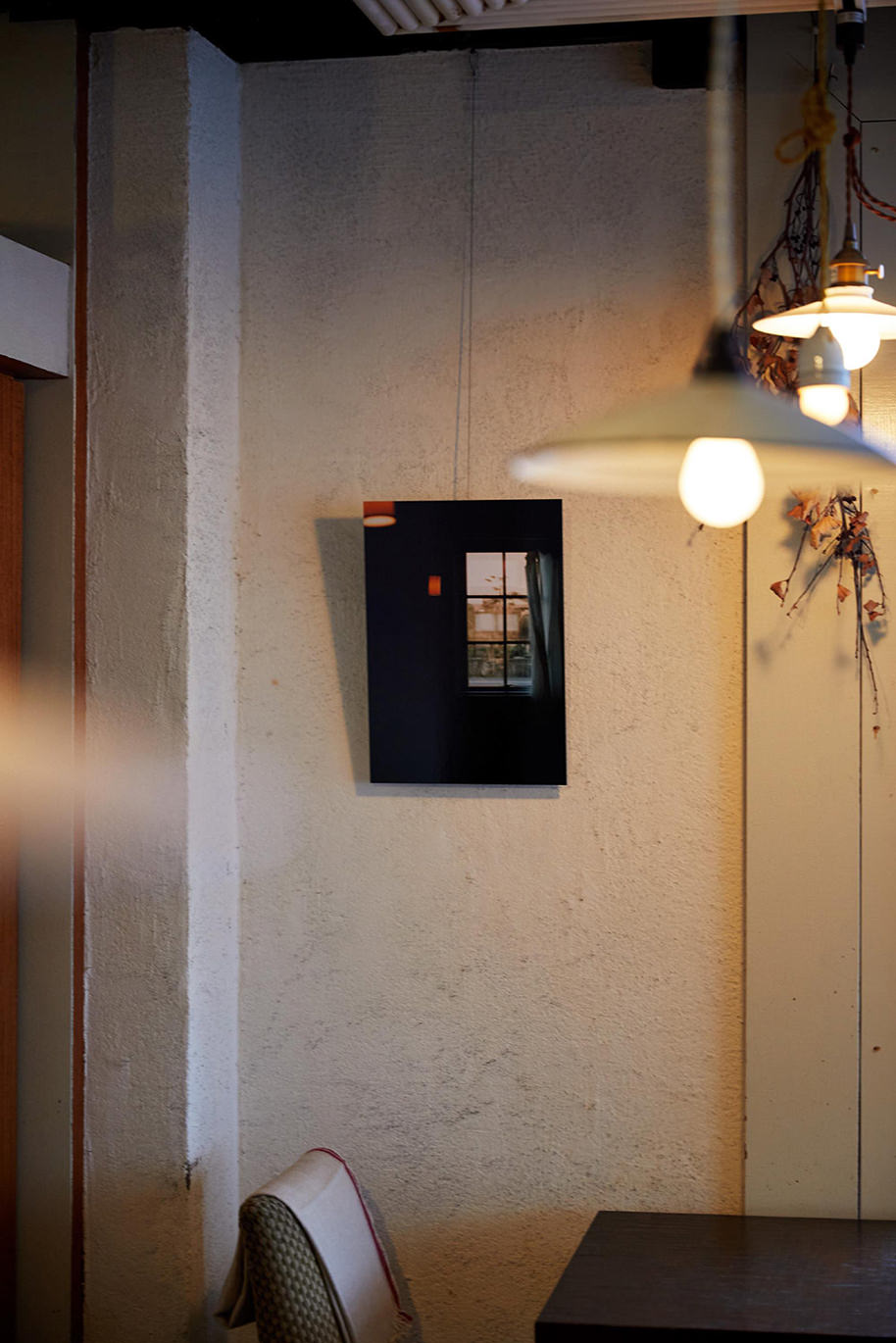 ペンダントライト越しの壁にワイヤーで吊るして飾られた、窓辺の風景写真のWALL DECOR