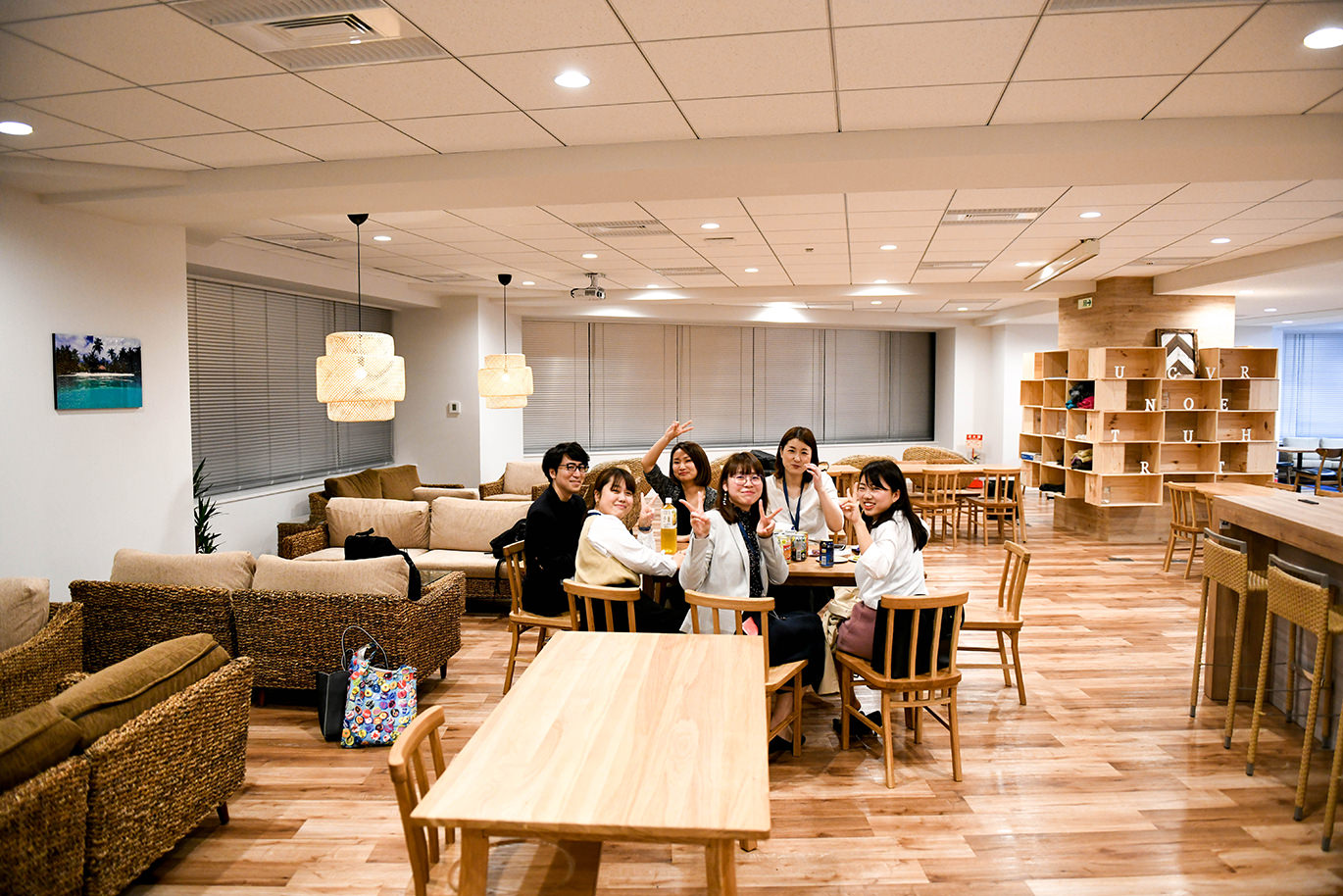 オフィスの共有スペースで、テーブルを囲み微笑む男女6名