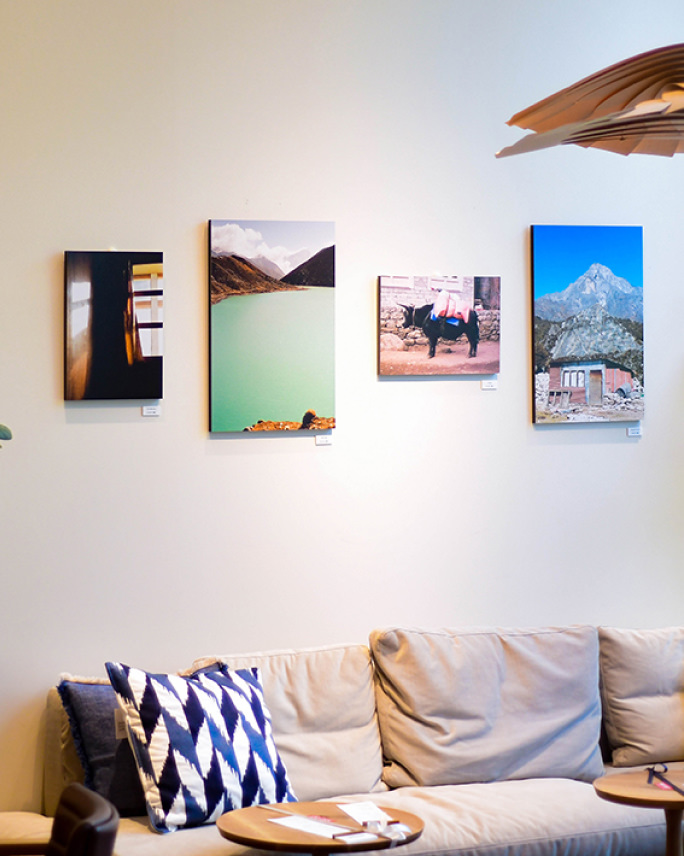 ソファがあるリビングのような空間の白い壁に、湖や山、牛の姿など、旅先の風景を切り取った4枚の写真パネルが横一列に飾られている。