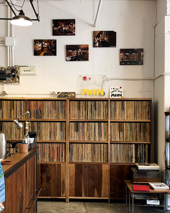 レコードがびっしりと並ぶ大きな木の棚の上の壁に、ジャズバーのような店内風景を写した5枚の写真パネルが飾られている。