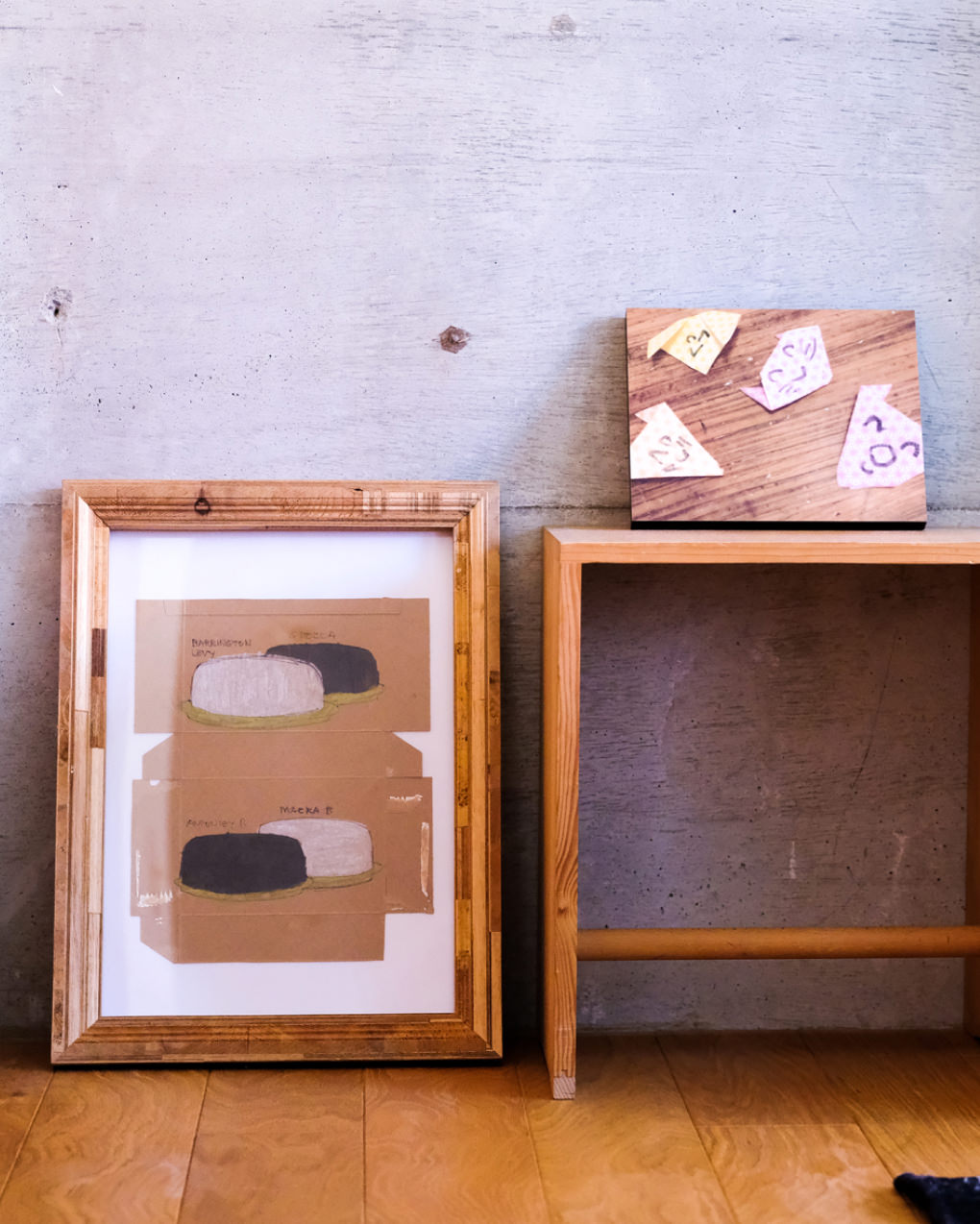 コンクリートの壁を背景に、床に置かれた額縁と、木の台に飾られた折り紙のWALL DECOR。