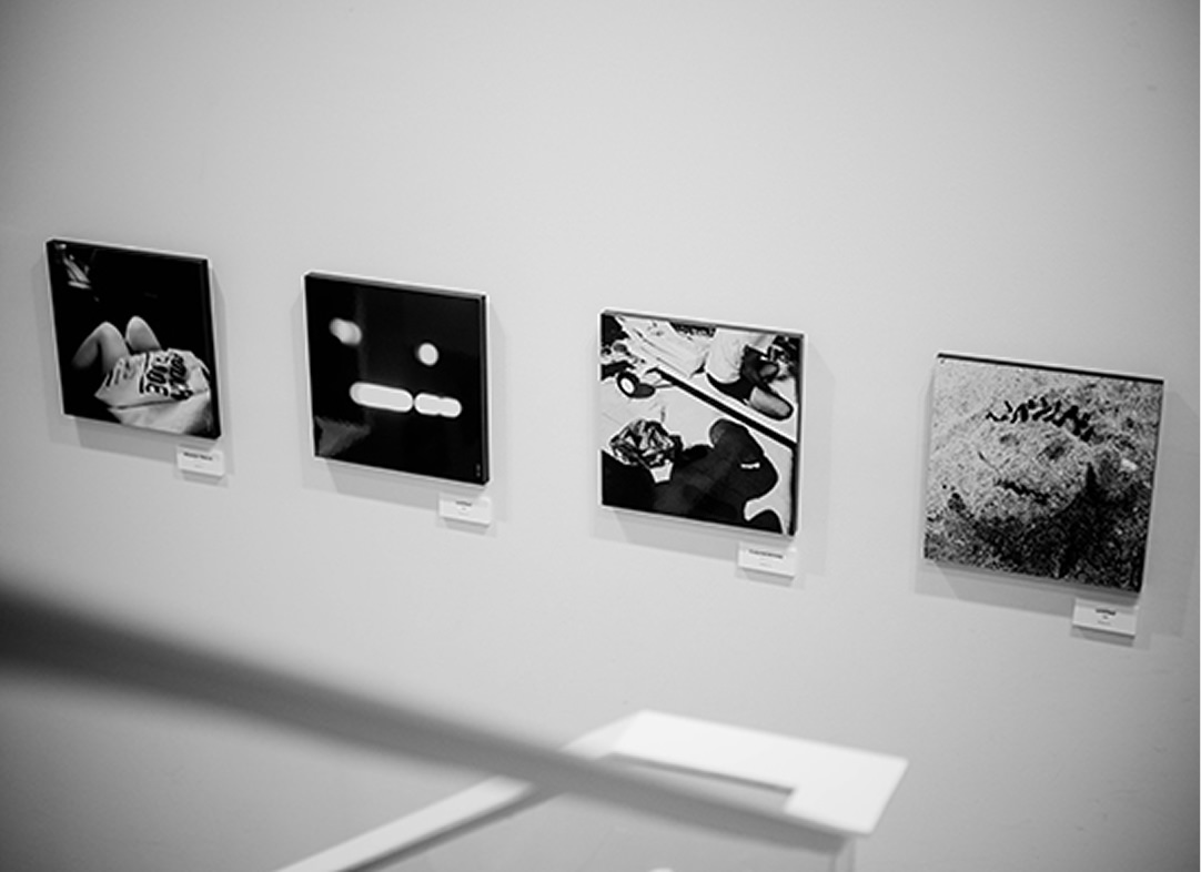 ギャラリーの白い壁面に、日常の断片や抽象的なイメージを捉えた4枚のモノクロ写真パネルが、横一列に並んで展示されている。