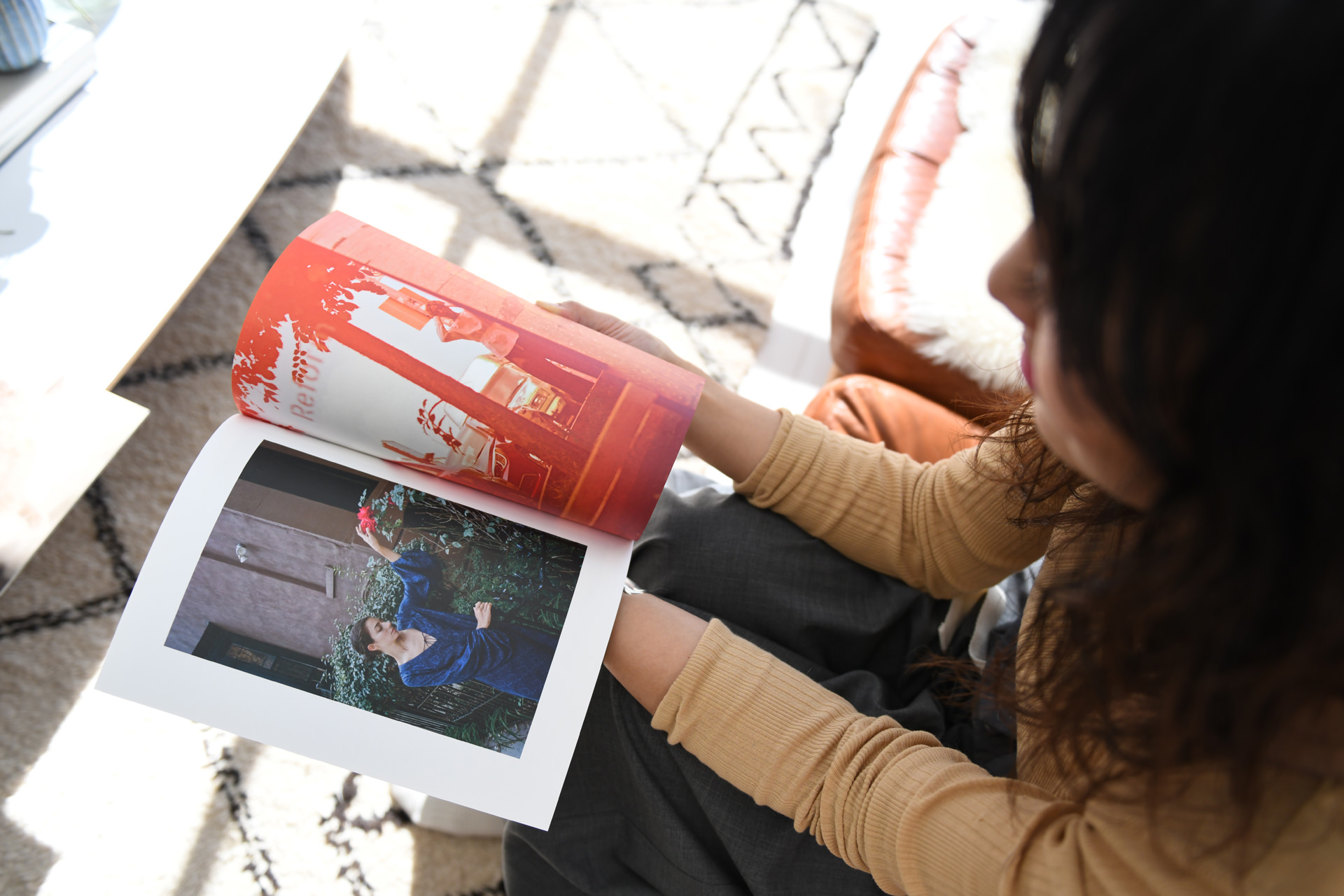 明るい光が差し込む部屋で、アート写真が掲載されたフォトブックをめくる女性の俯瞰ショット。手元にはドラマチックな色彩のポートレートが広げられている。