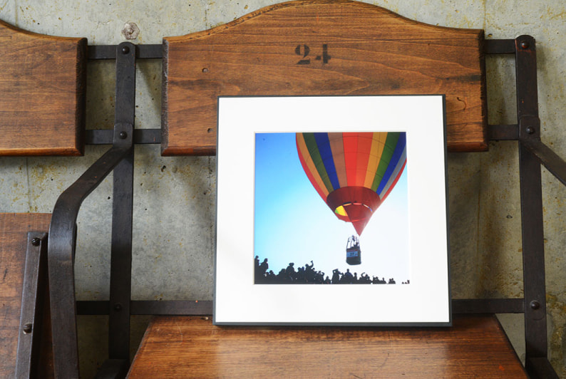 ヴィンテージ風の木製ベンチに飾られた、青空を飛ぶカラフルな熱気球の写真のWALL DECOR ギャラリー。