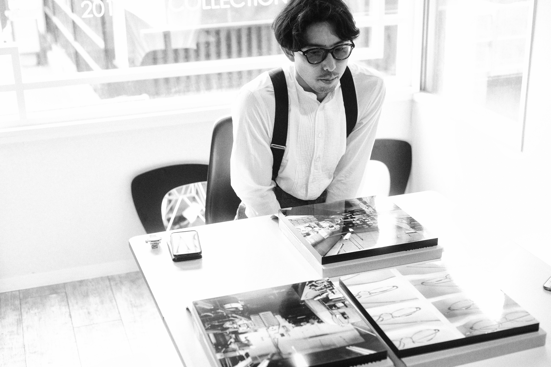 テーブルに並べられた複数のWALL DECORを前に、考え込むような表情の今泉悠。窓から光が差し込む明るい室内での風景。