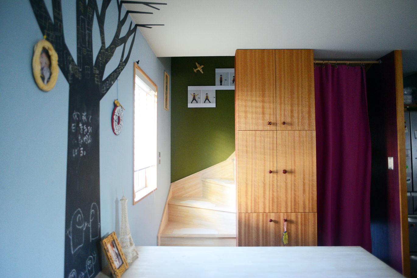 木のイラストが描かれた壁と、奥に階段が続くおしゃれな室内