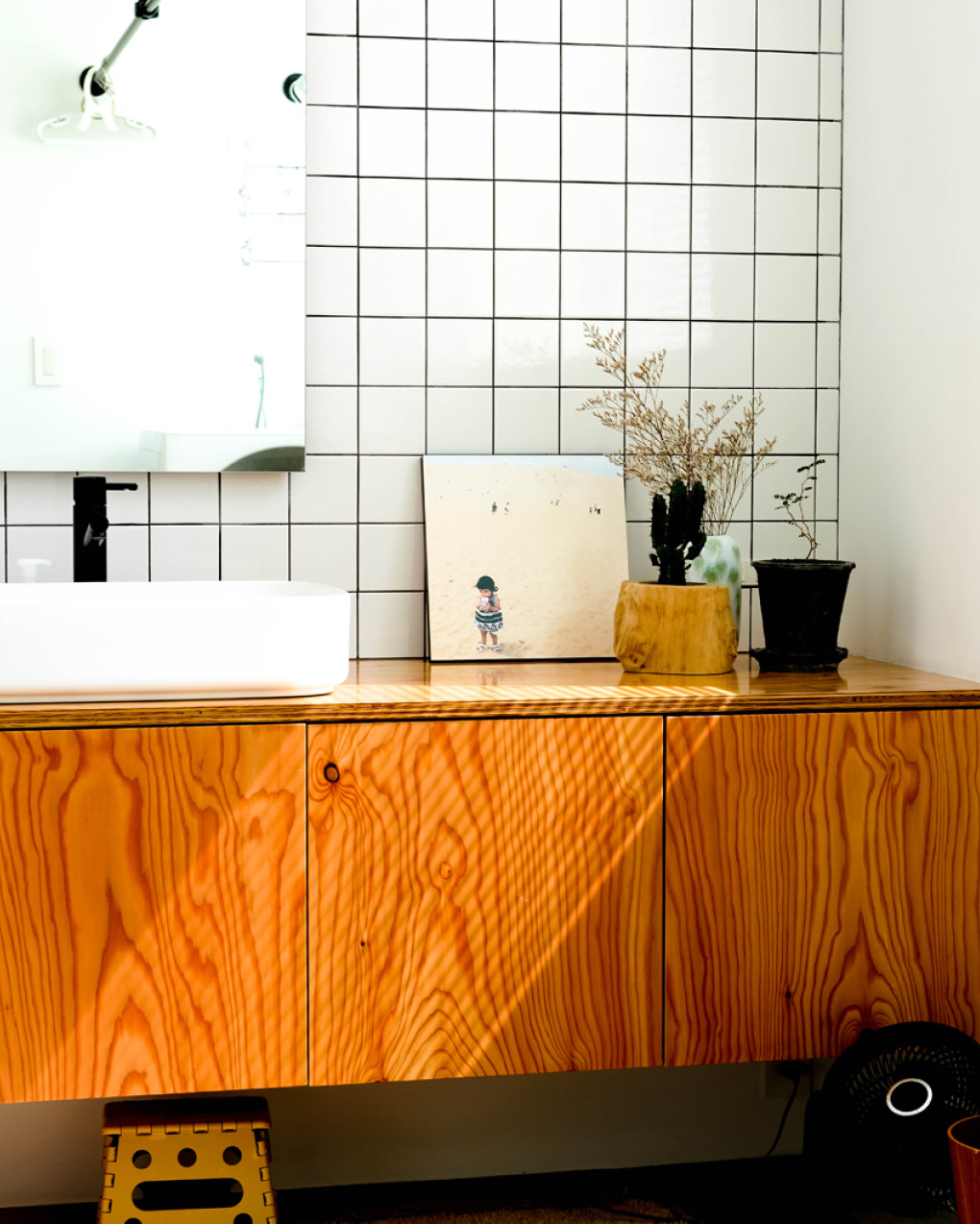 白いタイルの壁と木の洗面台に、砂浜に立つ子供の写真のWALL DECORと植物