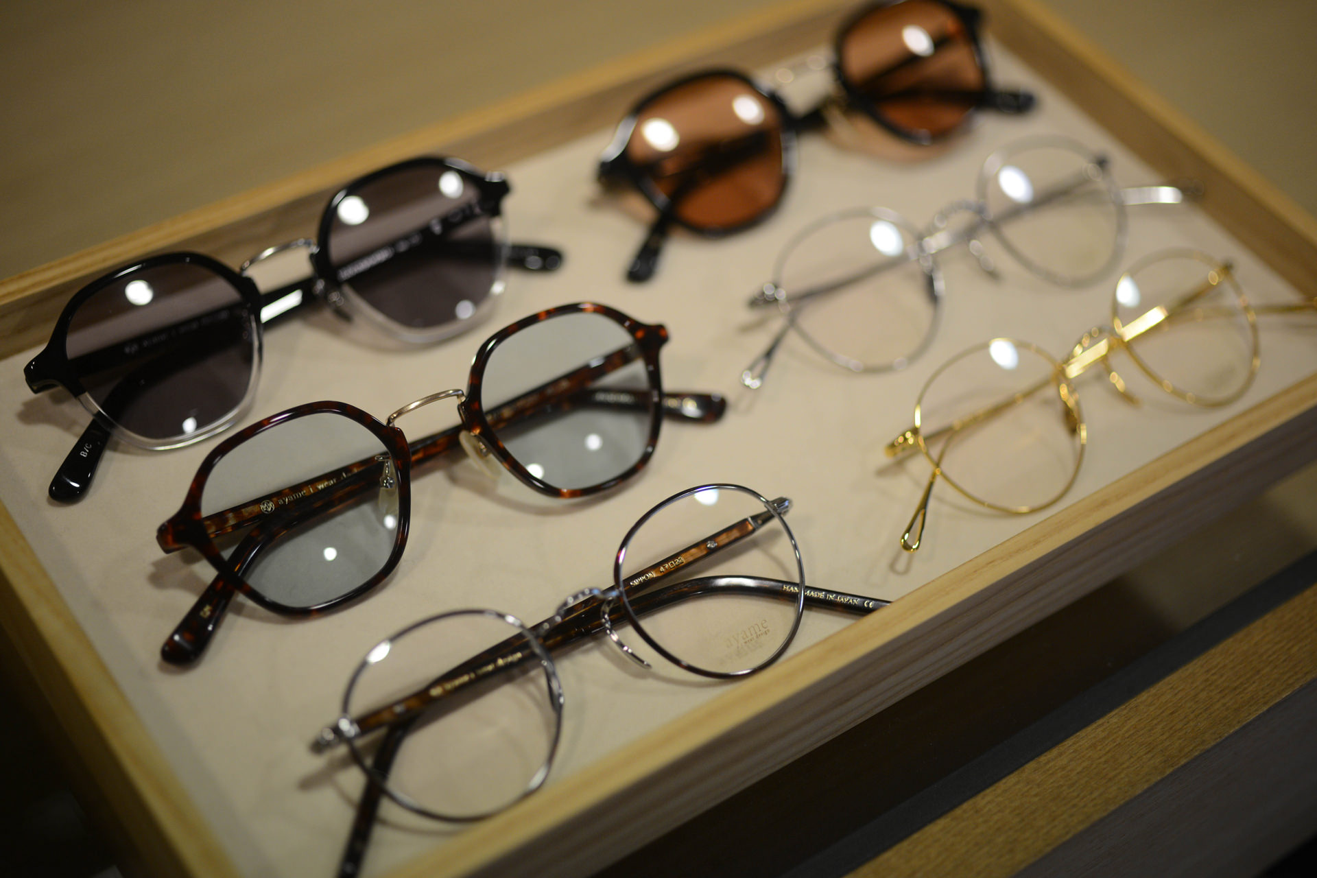 トレイに並べられた様々なデザインの眼鏡とサングラス。べっ甲柄のフレームや細いメタルの丸眼鏡などがディスプレイされている。