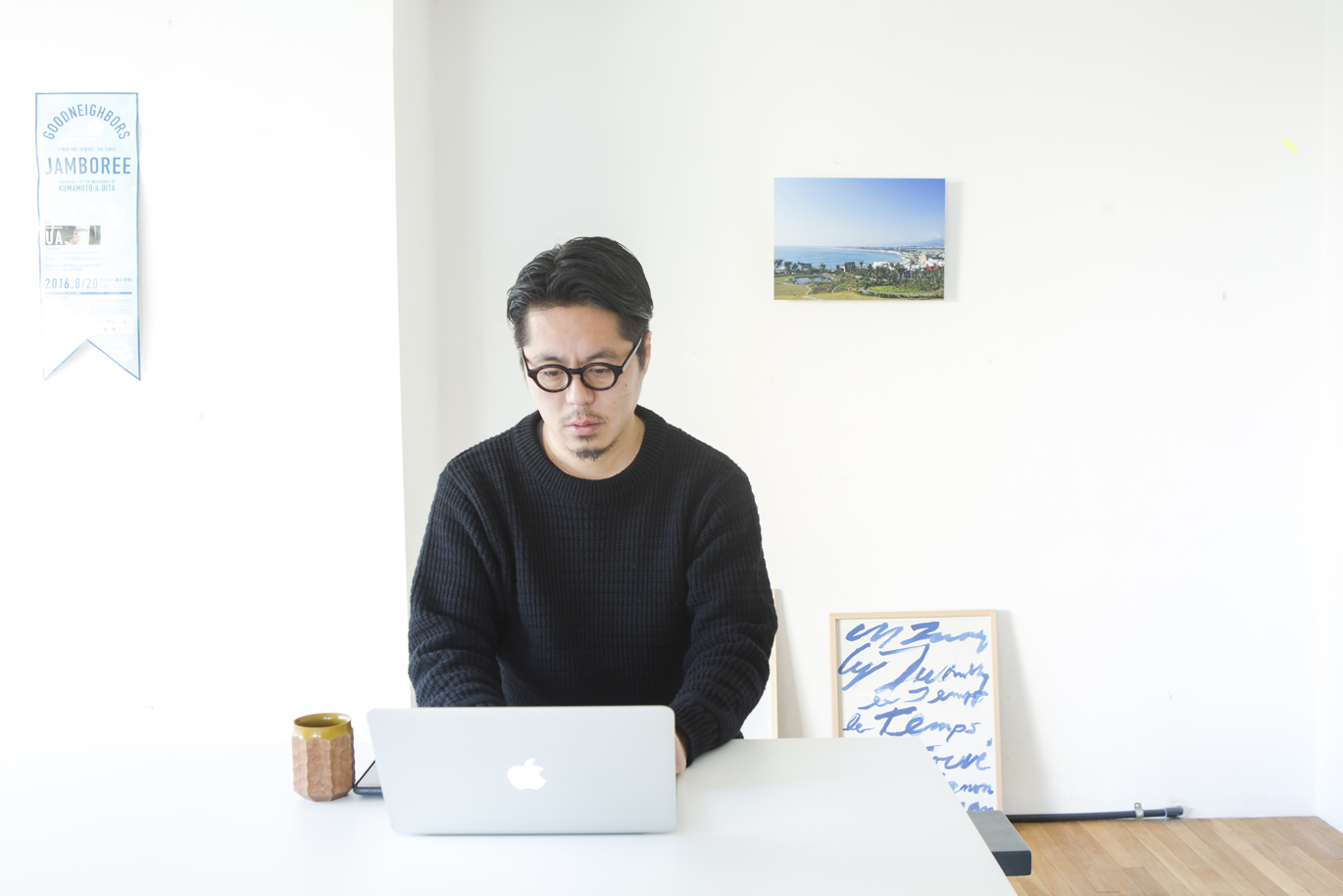 デスクで作業する男性と壁に飾られた風景写真