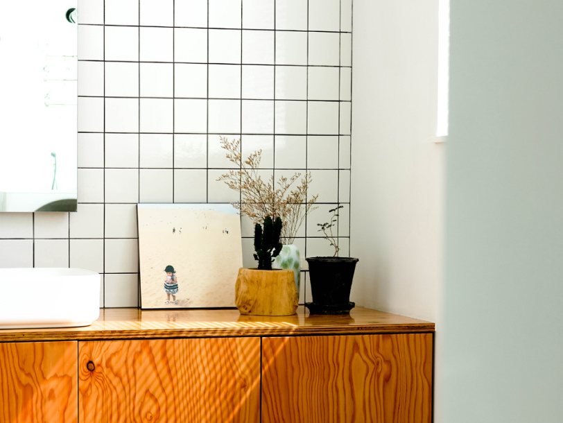 白いタイルの壁の前に観葉植物とともに飾られた、砂浜に佇む子供の写真のWALL DECOR カジュアル